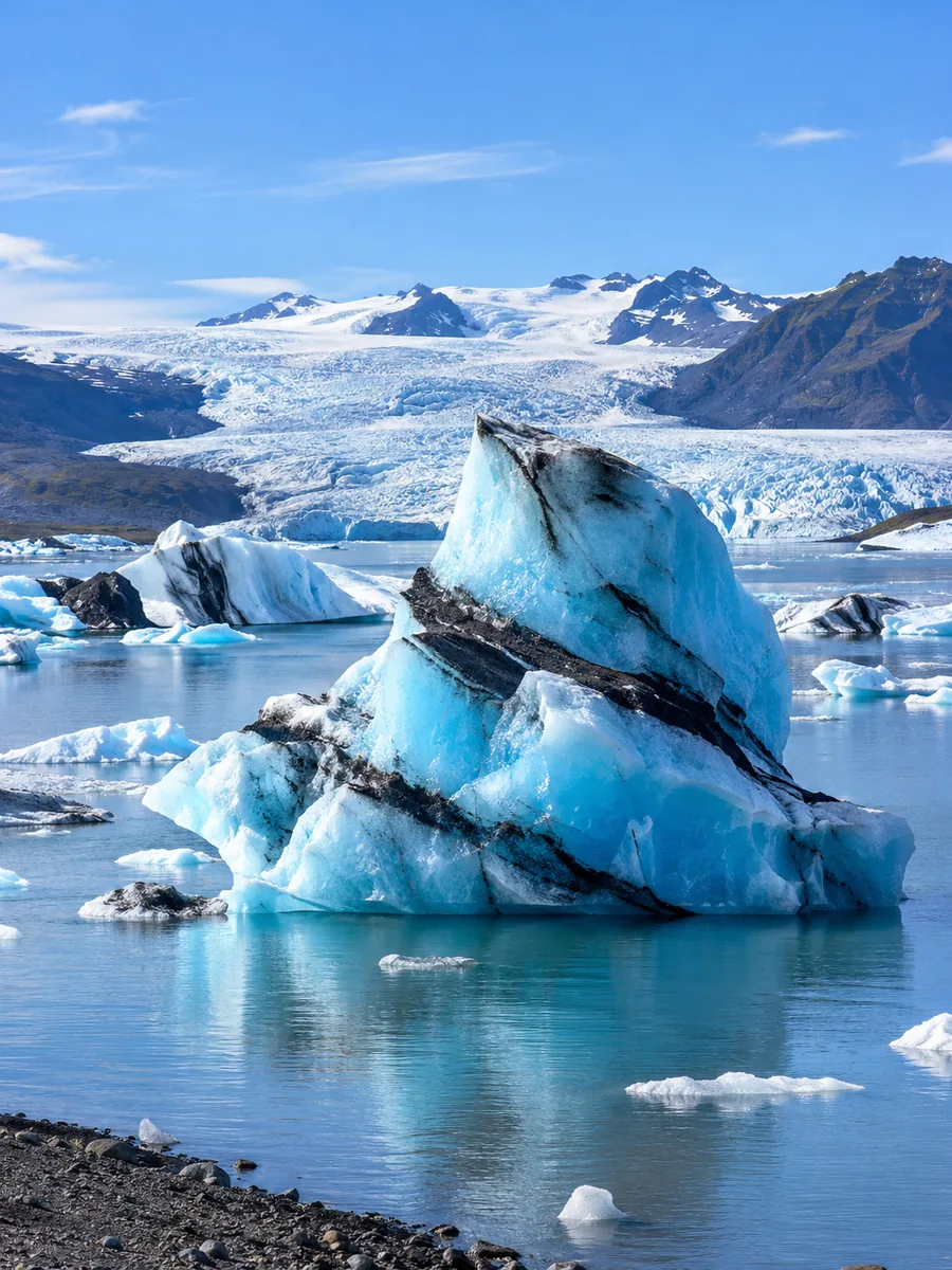 A big blue iceberg with black ash bands floating on the calm lagoon
