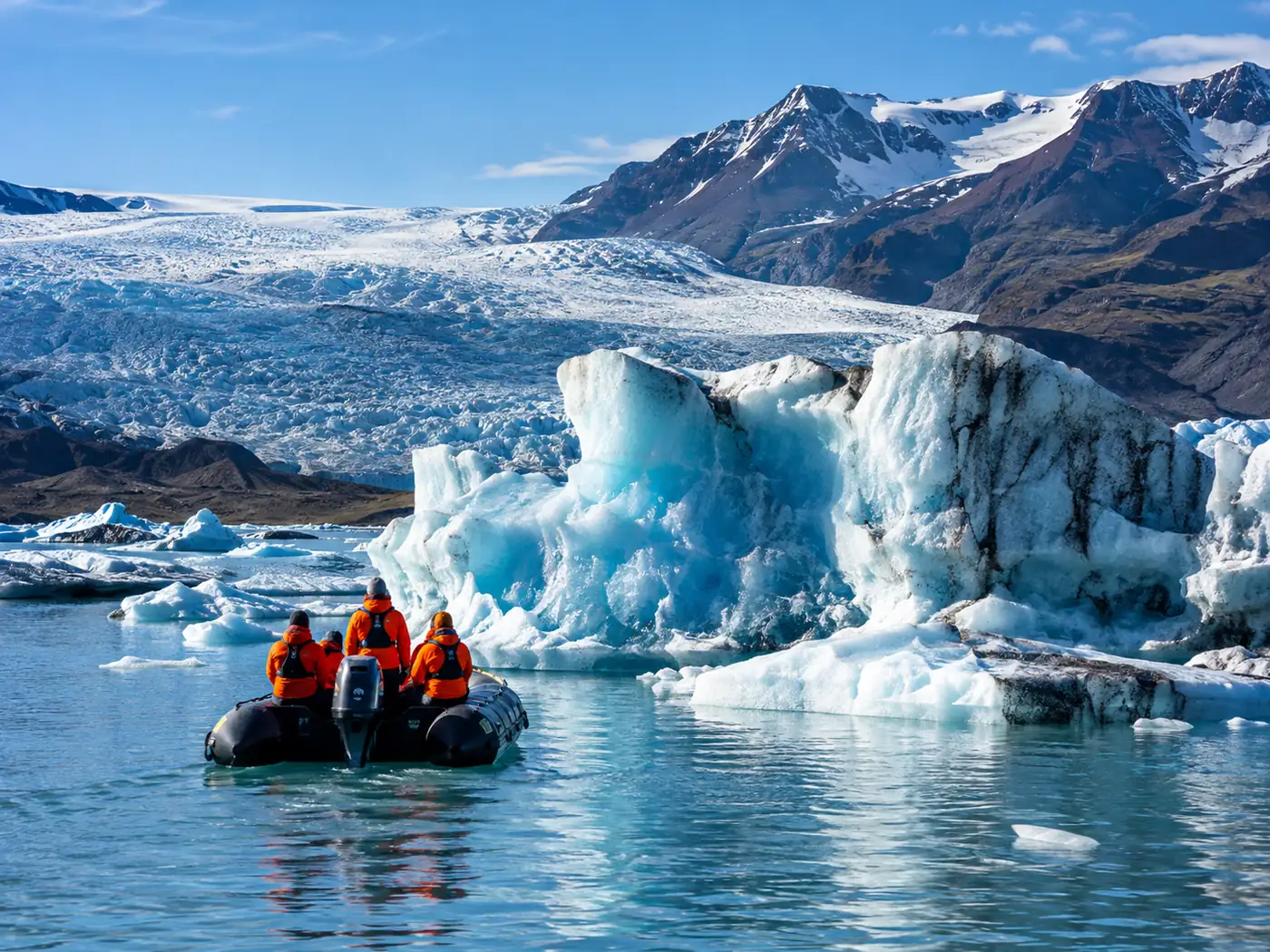 A Zodiac near a glacier face, passengers in orange suits seen from behind