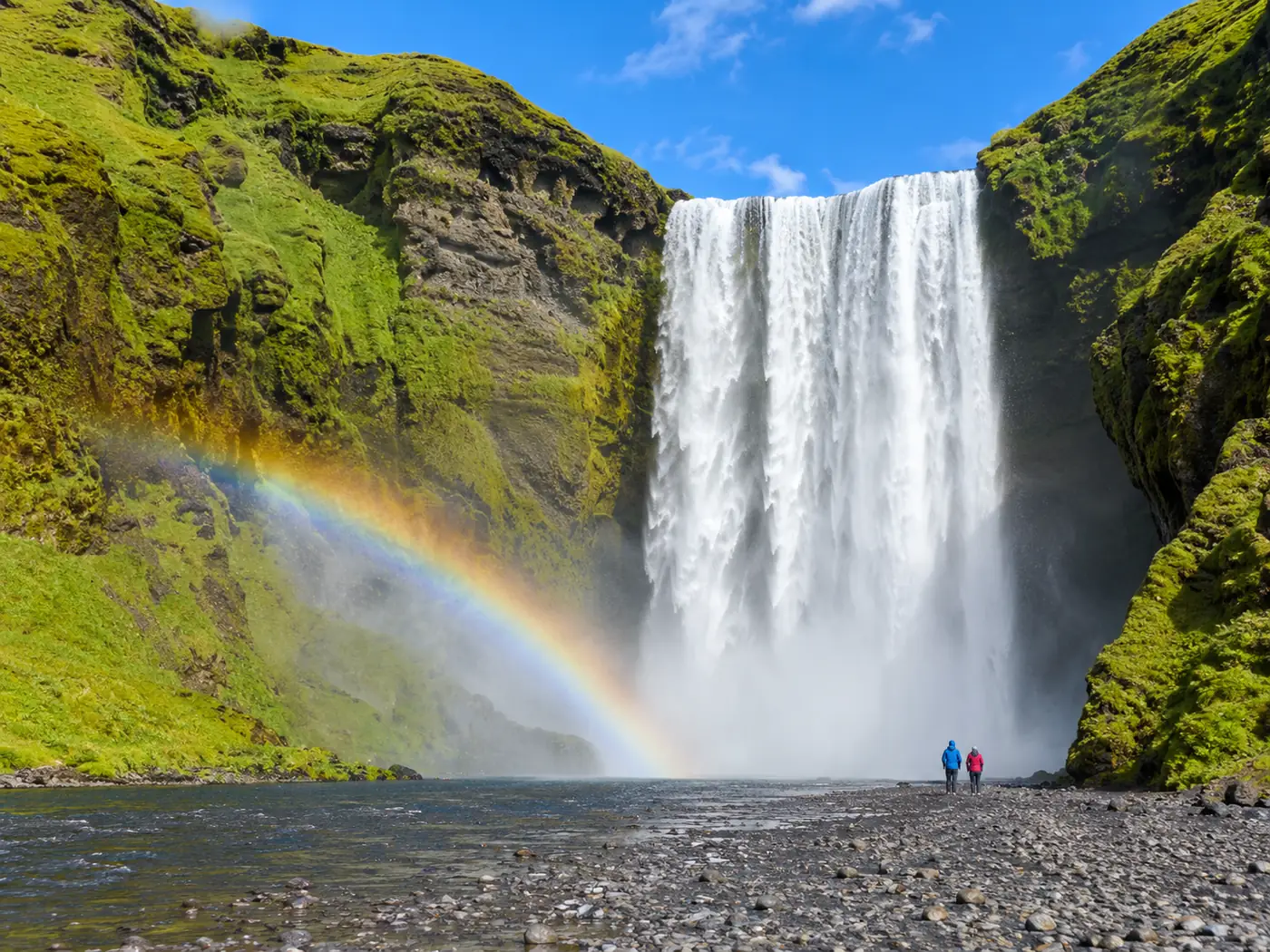 Skógafoss falling over a wide green cliff with a rainbow in the spray