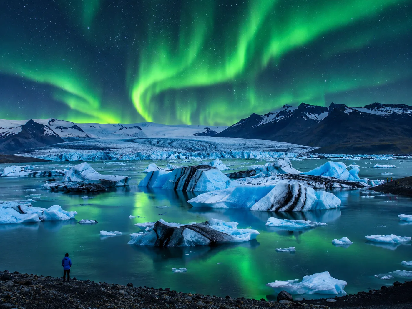 Green northern lights arcing over the glacier lagoon with dark icebergs in the water