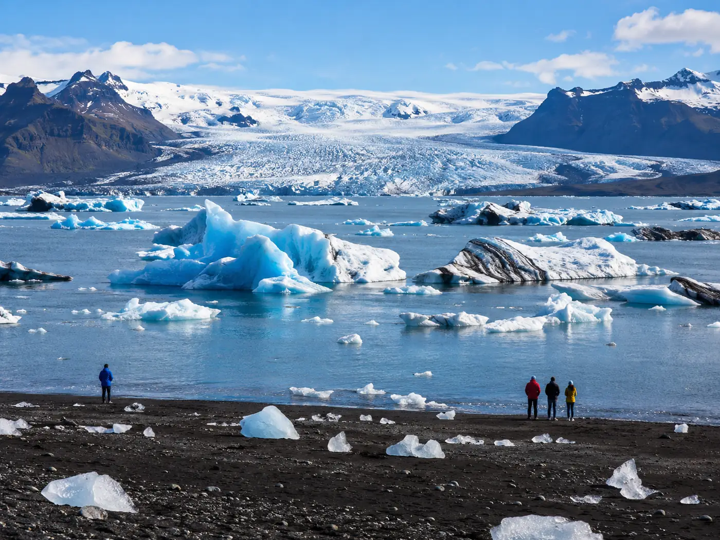 People standing far back from the surf on a black sand beach with ice